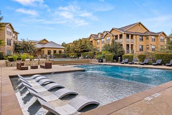 A large swimming pool with lounge chairs in front of apartment buildings.